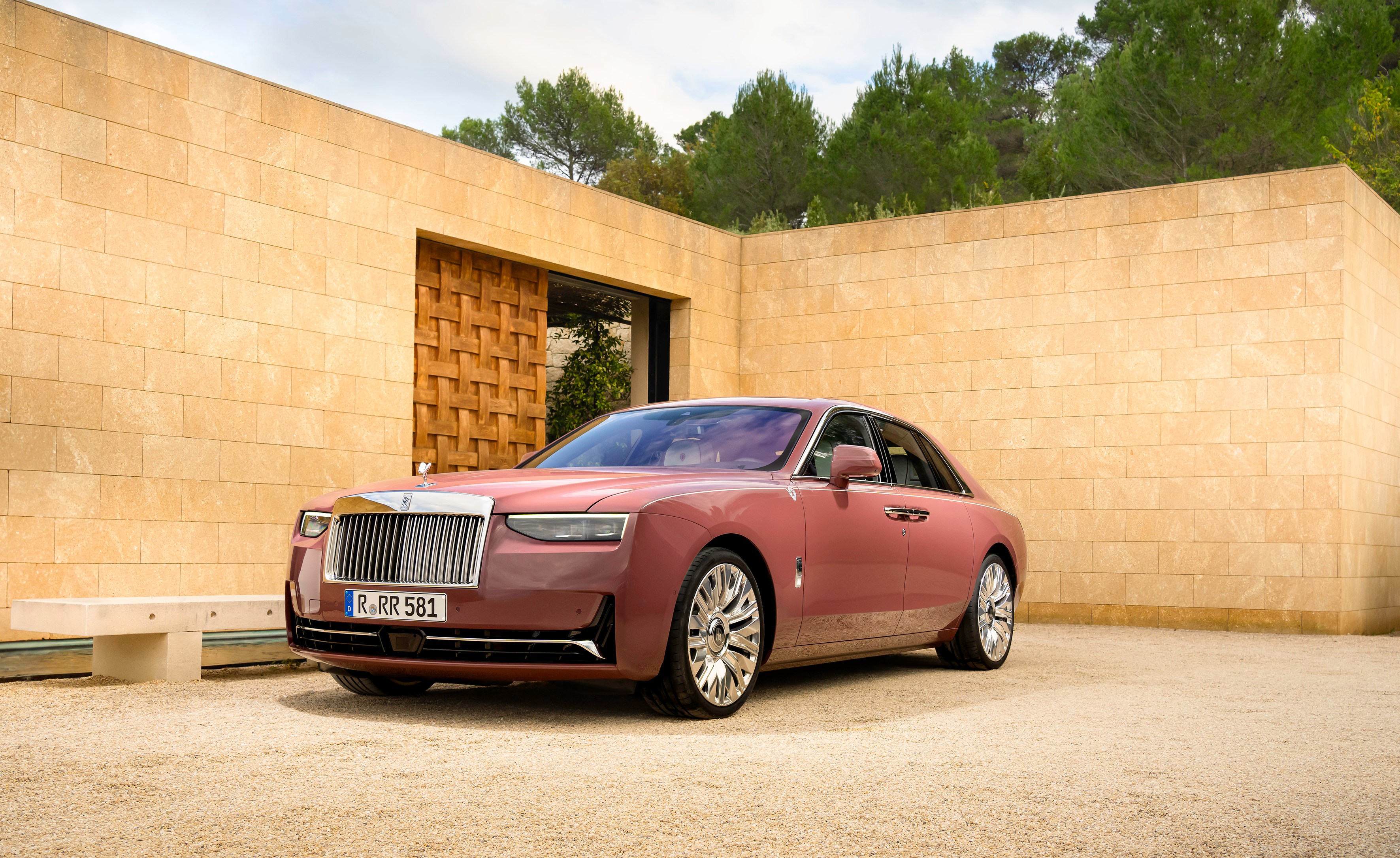 Rose gold Rolls Royce parked outside a modern building.
